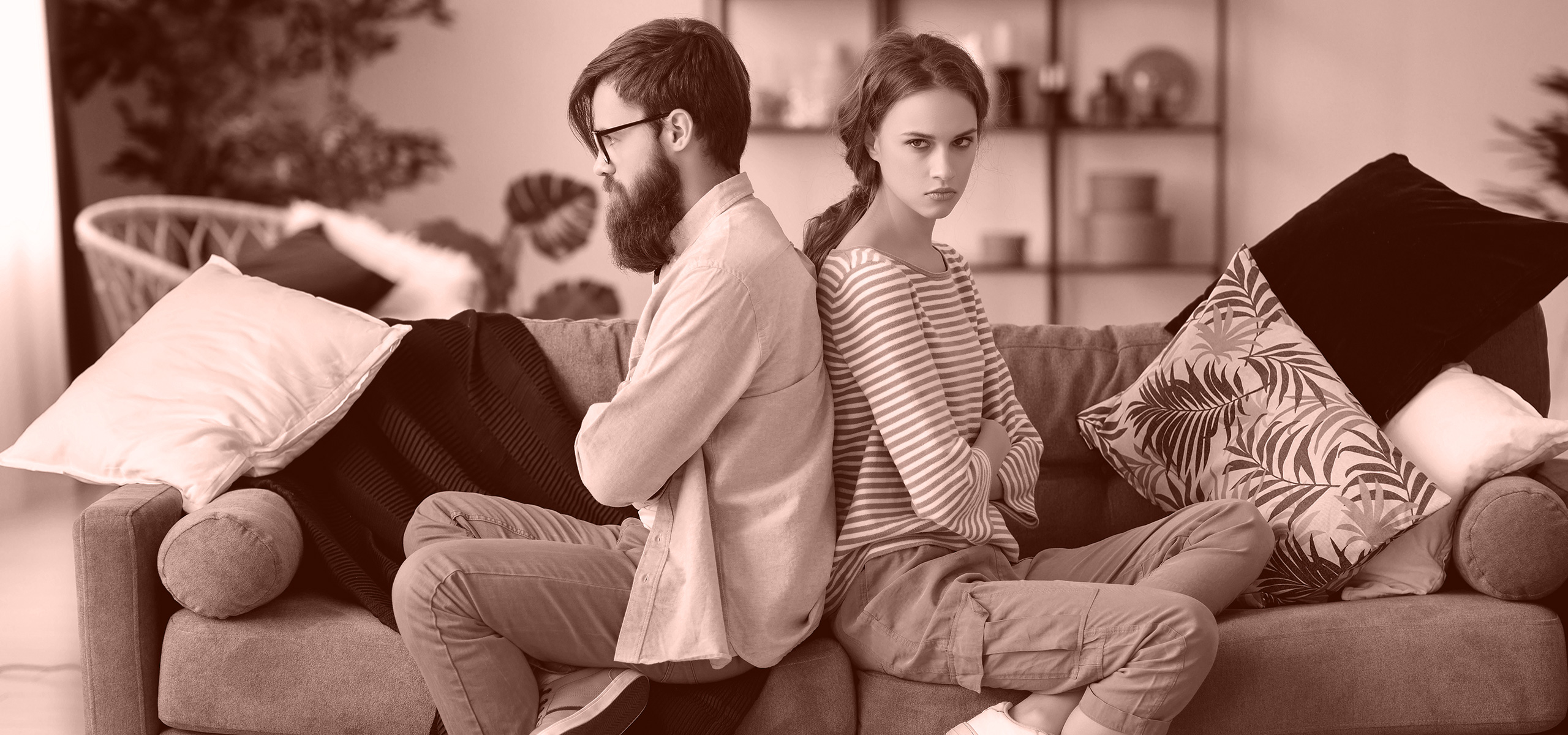 A couple are sitting back-to-back on the sofa, arguing